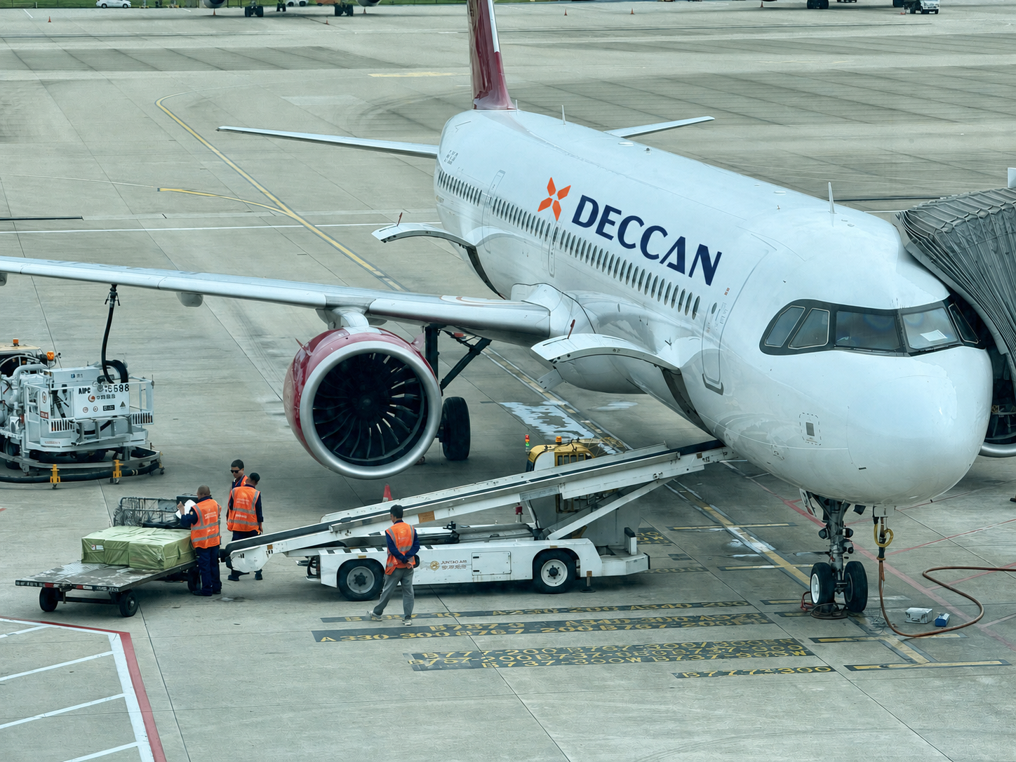 Airport ground crew loading cargo beside a Deccan-branded aircraft